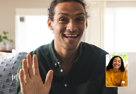 A man smiles and waves during a video call, with a small window showing a woman also smiling and waving at him.